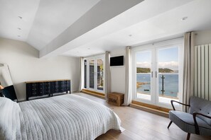 A bedroom with a large bed, a TV, and a view of the sea. - Cawsand Waterfront House With Pool (Torpoint)