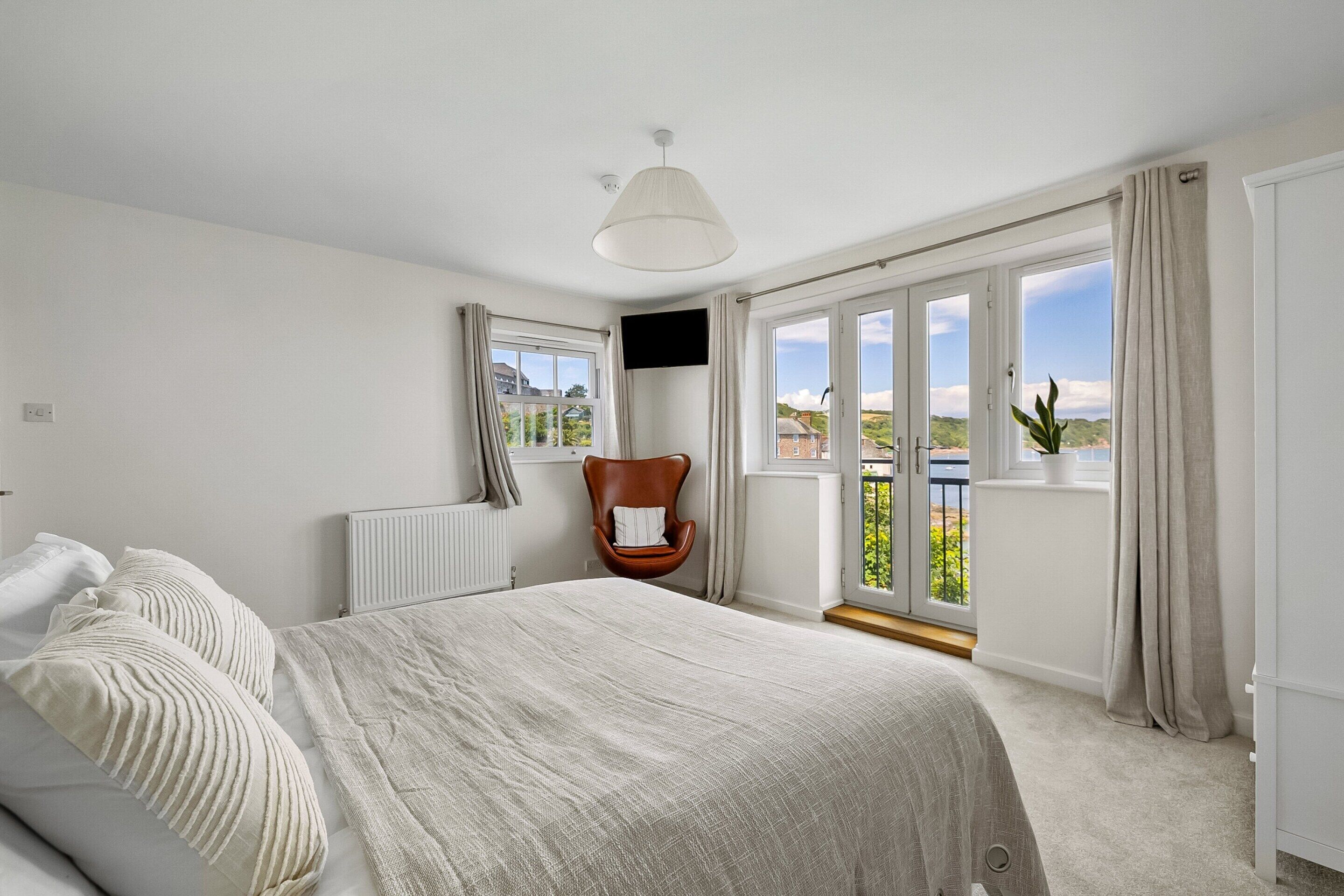 Une chambre à coucher comprenant un lit, une chaise, un radiateur, un téléviseur et de grandes fenêtres donnant sur un beau paysage.