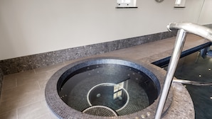 Uma banheira de hidromassagem circular com interior revestido em azulejos e corrimão de metal.