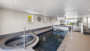 Uma piscina interior moderna com hidromassagem, paredes de vidro transparente e vista para o exterior.