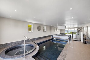 A modern indoor swimming pool with a jacuzzi, clear glass walls, and a view of the outdoors. - Cawsand Waterfront House With Pool (Torpoint)