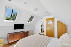 A bedroom with a large bed, a TV, a wooden wardrobe, and a door with a circular window. - Cawsand Waterfront House With Pool (Torpoint)