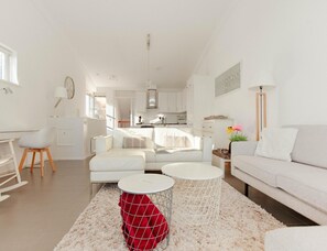 A modern living room with a white sofa, a dining area, and a kitchen in the background. - Villa With Panoramic Water Views (Makkum)