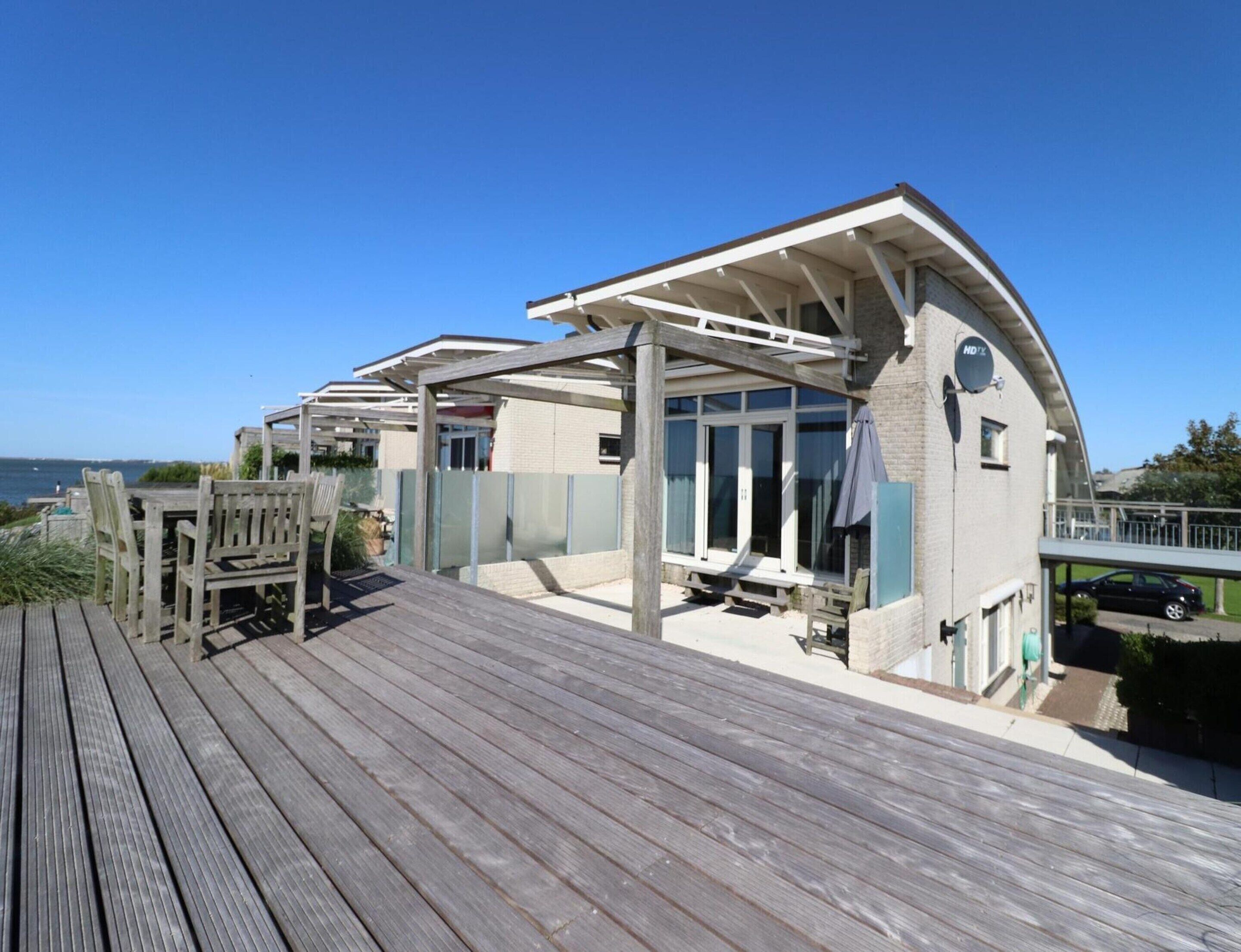 A coastal property with a wooden deck, a covered outdoor seating area, and a view of the sea.