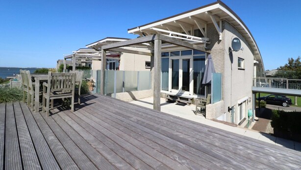 A coastal property with a wooden deck, a covered outdoor seating area, and a view of the sea. - Villa With Panoramic Water Views (Makkum)