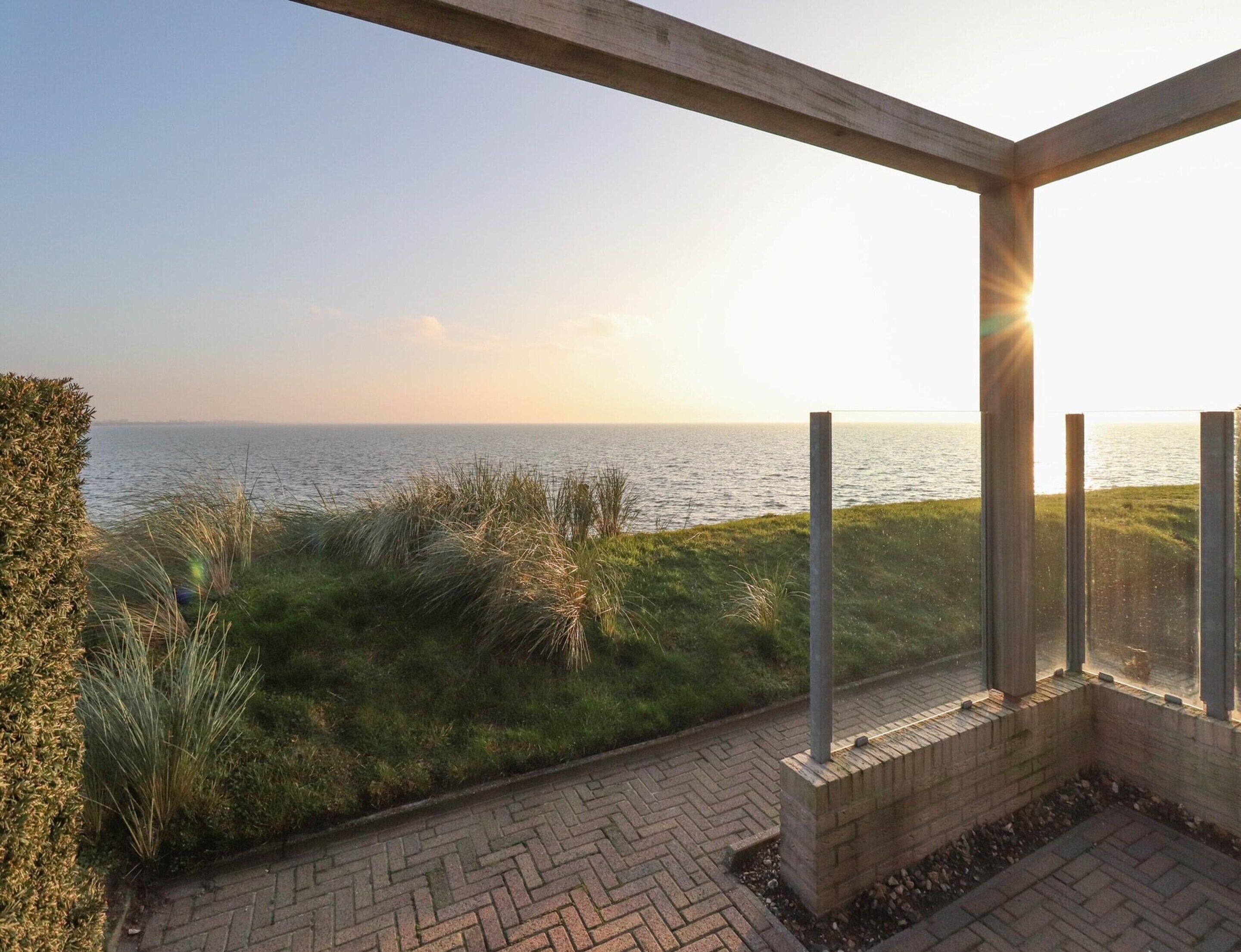 A patio with a view of the sea, a brick pathway, and a wooden pergola structure.