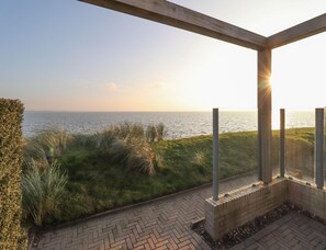 A patio with a view of the sea, a brick pathway, and a wooden pergola structure. - Villa With Panoramic Water Views (Makkum)