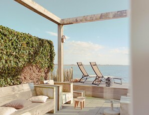 An outdoor seating area with a wooden bench, two lounge chairs, and a view of the water. - Villa With Panoramic Water Views (Makkum)