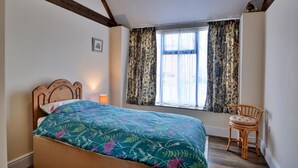 A bedroom with a bed, a chair, a window with floral curtains, and a picture on the wall. - Family Cottage Near Wilsthorpe Beach (Driffield)