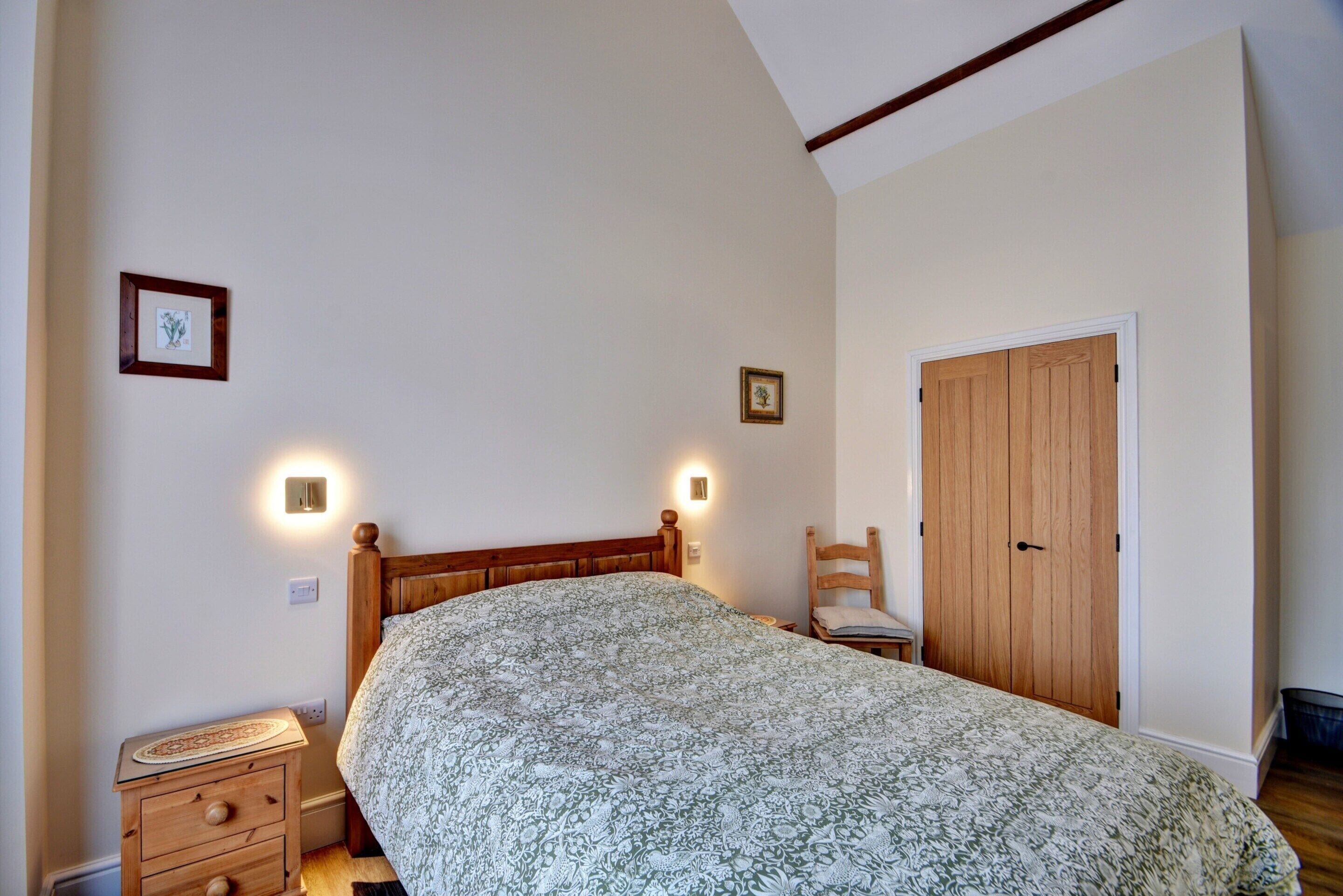 A bedroom with a wooden bed, two bedside lamps, a wooden nightstand, a wooden chair, and a wooden wardrobe.