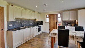 A modern kitchen with white cabinets, a black marble backsplash, and a dining area with a table and chairs. - Family Cottage Near Wilsthorpe Beach (Driffield)