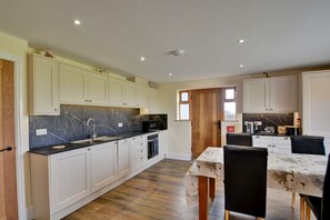 A modern kitchen with white cabinets, a black marble backsplash, and a dining area with a table and chairs. - Family Cottage Near Wilsthorpe Beach (Driffield)