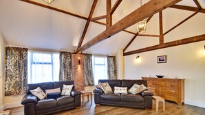 A spacious living room with two sofas, a wooden cabinet, and a brick fireplace. - Family Cottage Near Wilsthorpe Beach (Driffield)