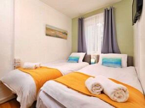 A hotel room with two beds, a painting on the wall, and a window with curtains. - Cosy Cornwall Bungalow for 4 (St Ives)