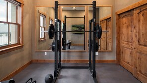 A gym with a squat rack, weight plates, and a mirror reflecting the room. - Luxury Downtown Condo with Private Balcony | 5th St. Penthouse (Steamboat Springs)