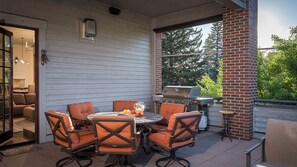 Eine Terrasse im Freien mit einem runden Tisch, Stühlen, einem Grill und Blick auf Bäume.