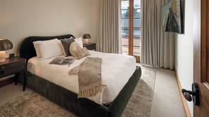 Un letto rifatto con cura, con una testiera scura, numerosi cuscini, una coperta a maglia e una lampada da comodino su un comodino in legno.