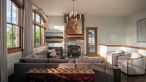 A living room with a stone fireplace, a large flat-screen TV, and a sectional sofa. - Luxury Downtown Condo with Private Balcony | 5th St. Penthouse (Steamboat Springs)