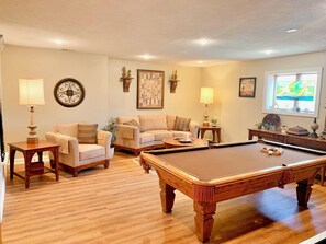 A living room with a pool table, two sofas, and a window with a view.