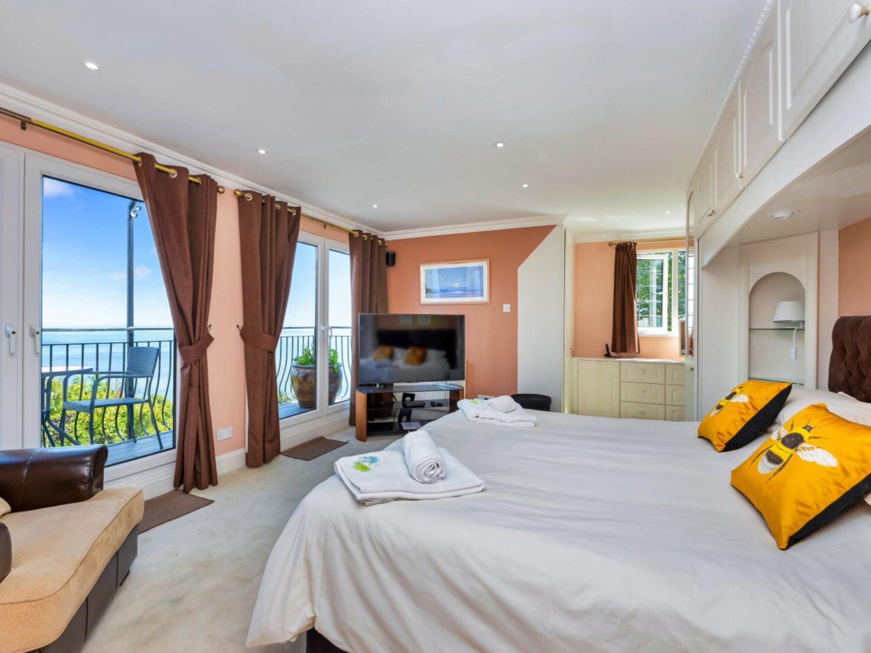 A hotel room with a large bed, a TV, a desk, and a balcony with a view.