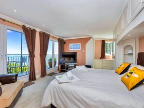 A hotel room with a large bed, a TV, a desk, and a balcony with a view. - Ocean-view Manor With Jacuzzi (Torquay)