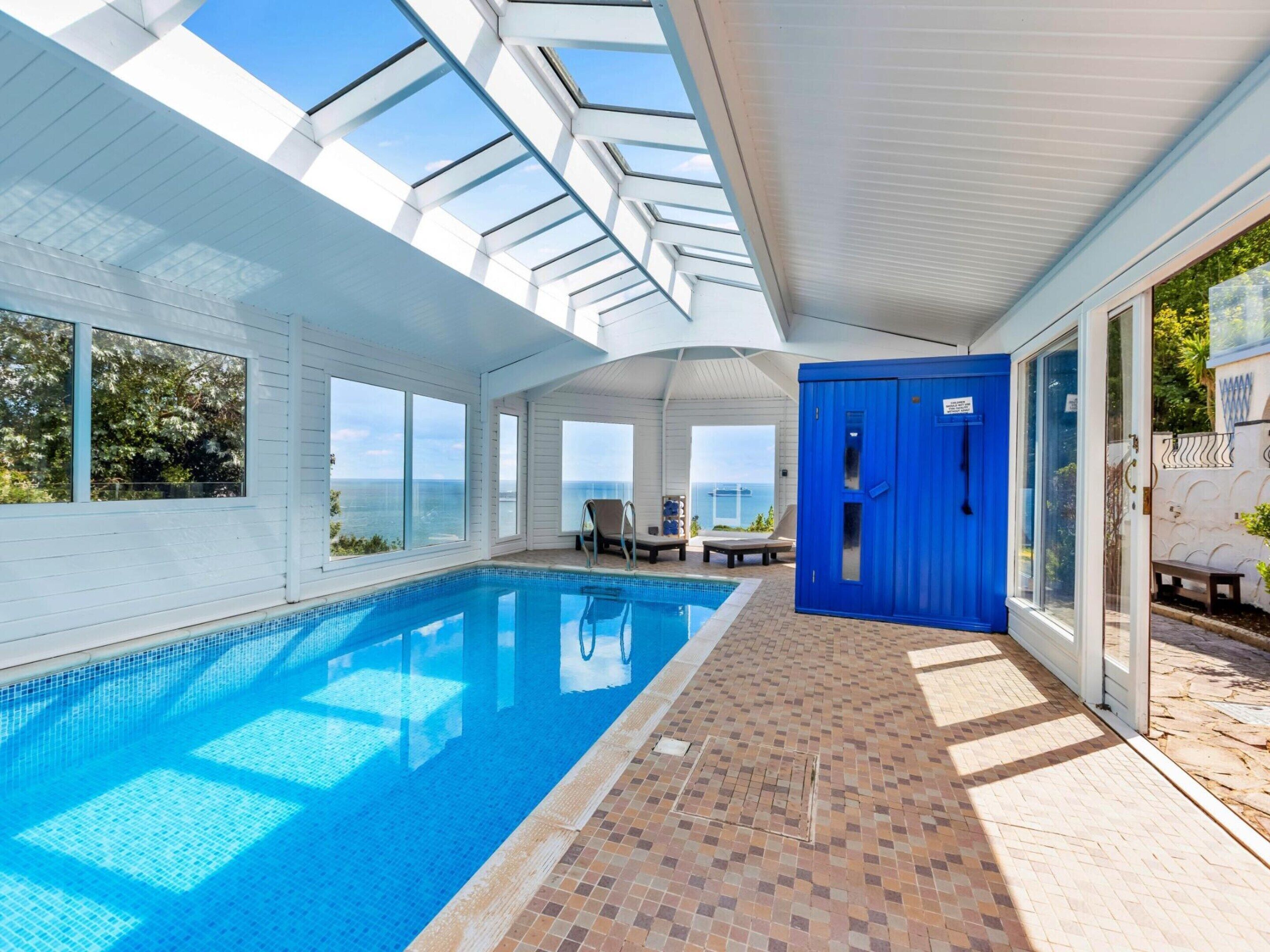 A swimming pool with a clear view of the sea, a blue door, and a tiled floor.