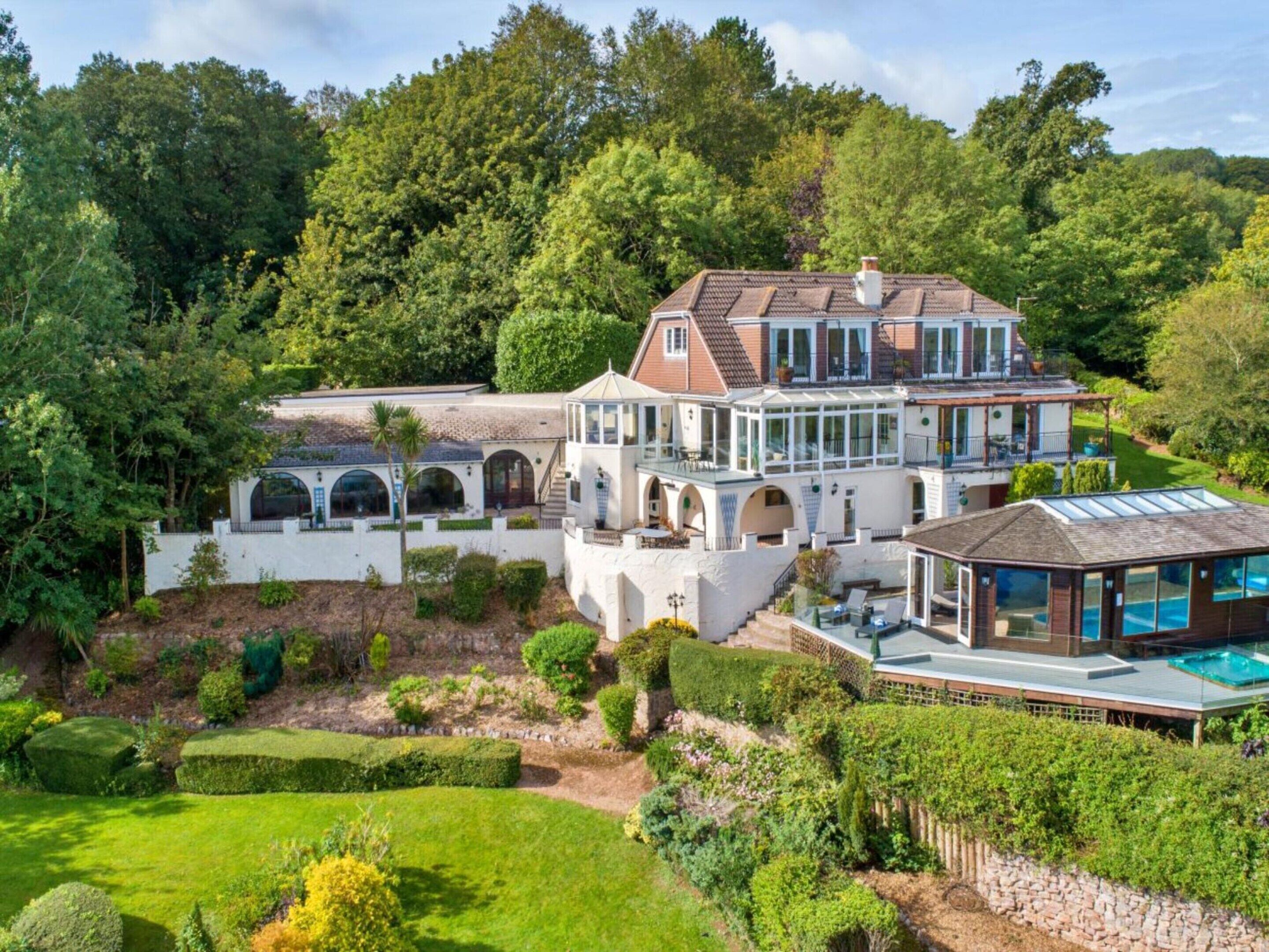 A large, multi-story house with a swimming pool, surrounded by lush greenery and a well-maintained garden.