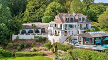 A large, multi-story house with a swimming pool, surrounded by lush greenery and a well-maintained garden.