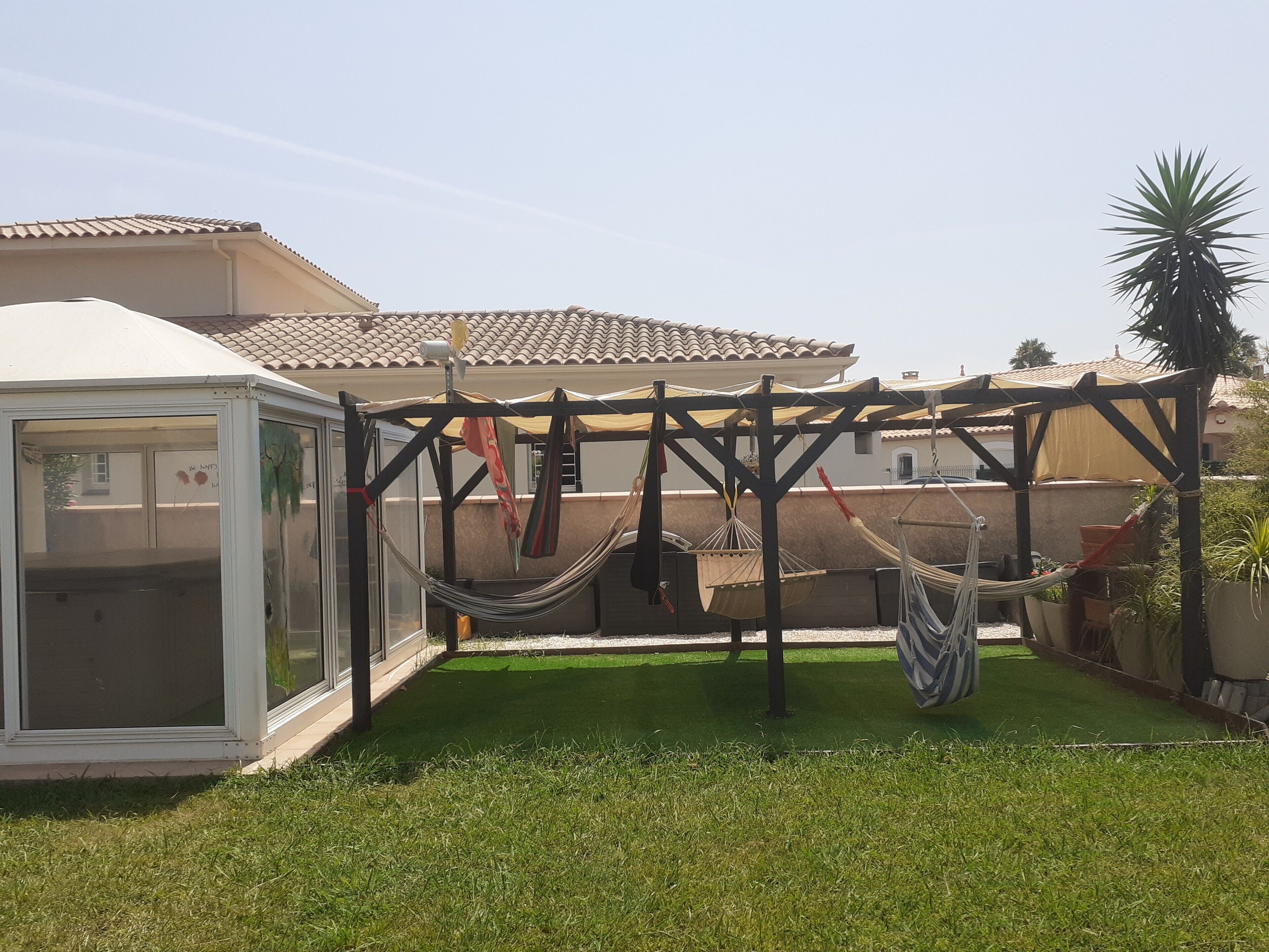 A covered outdoor area with a hammock, a glass enclosure, and a tiled roof.