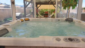 Un bain à remous avec une terrasse en bois et une pergola au-dessus.