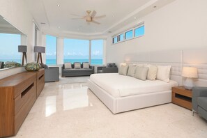 A modern bedroom with a large bed, a desk, and a view of the ocean. - Breathtaking Oceanfront Luxury Penthouse! (San Miguel de Cozumel)