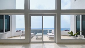 Ein modernes Interieur mit großen Fenstern, einer Schiebeglastür, weißen Möbeln und Topfpflanzen.
