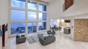 Un'ampia zona giorno con ampie finestre vista mare, un'area pranzo con tavolo rotondo e una cucina con parete a contrasto in pietra.
