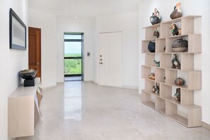 A modern interior with a hallway leading to a door, a wooden shelf with decorative items, and a framed picture on the wall. - Breathtaking Oceanfront Luxury Penthouse! (San Miguel de Cozumel)