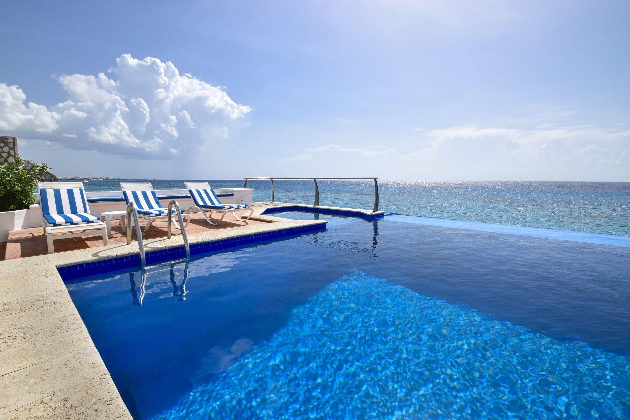 A infinity pool with clear blue water, lounge chairs, and a view of the ocean.