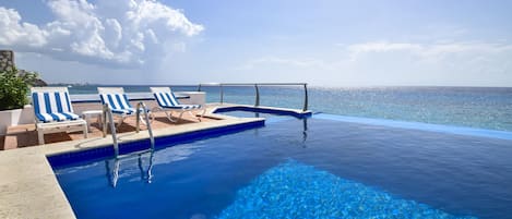 A infinity pool with clear blue water, lounge chairs, and a view of the ocean.