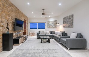 Ein modernes Wohnzimmer mit Steinwand, einem grauen Ecksofa, einem Flachbildfernseher und Kunstwerken an den Wänden.