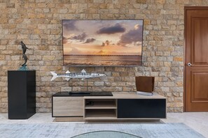 Ein Zimmer mit einer Steinwand, einer Holztür, einem an der Wand befestigten Fernseher, einem Holzschrank und einer Fischskulptur.