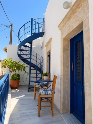 Eine Wendeltreppe führt zu einer oberen Ebene, eine blaue Tür und ein Balkon mit Tisch und Stühlen.