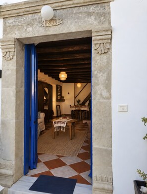 Uma entrada com porta azul, área de jantar com mesa e cadeiras, e escada que leva a um andar superior.