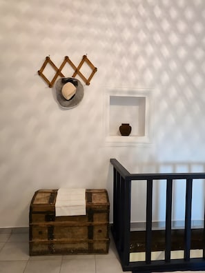 A room with a wooden chest, a wall-mounted shelf with a bowl, and a black railing. - Welcome to Sivas 1896 House – Authentic Cretan Hospitality in a Restored Historic Home (Sivas)