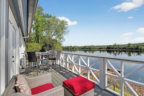 Eine Terrasse mit Gartenmöbeln, einem Geländer und Blick auf einen See.