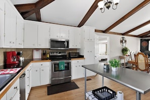 A modern kitchen with white cabinets, stainless steel appliances, and a wooden ceiling.