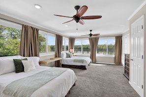 Ein Hotelzimmer mit zwei Betten, einem Deckenventilator, Blick auf einen See und einem Schminktisch.