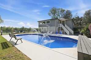 A swimming pool with a wooden deck, lounge chairs, and a small building with a staircase.