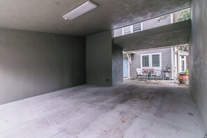 Ein geräumiger, noch unvollendeter Innenraum mit Betonboden und -wänden, einem kleinen Tisch mit Stühlen und Blick auf ein Nachbarhaus.