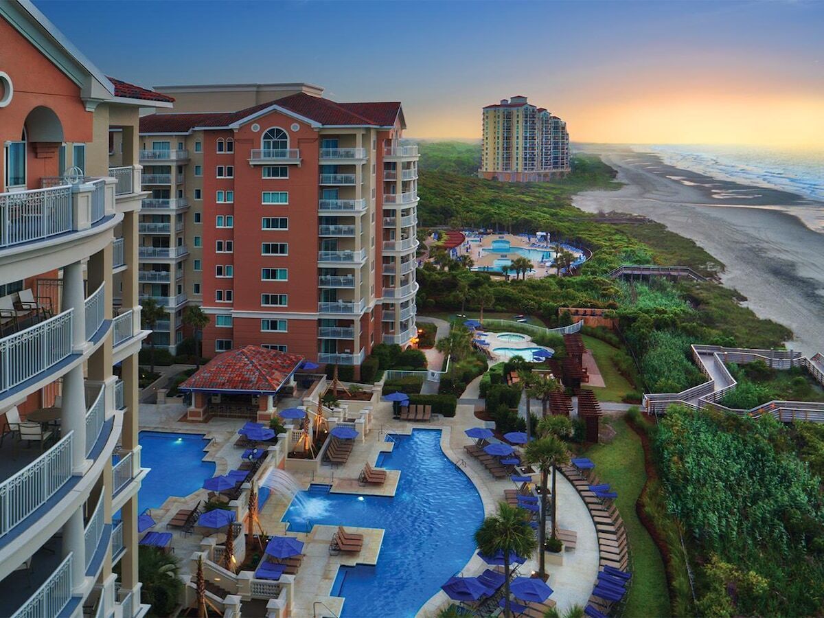 A hotel with multiple floors, a swimming pool, and a view of the beach.