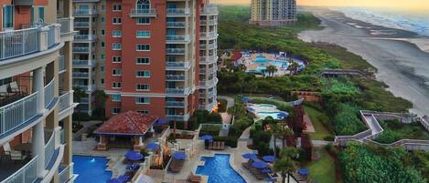 A hotel with multiple floors, a swimming pool, and a view of the beach.