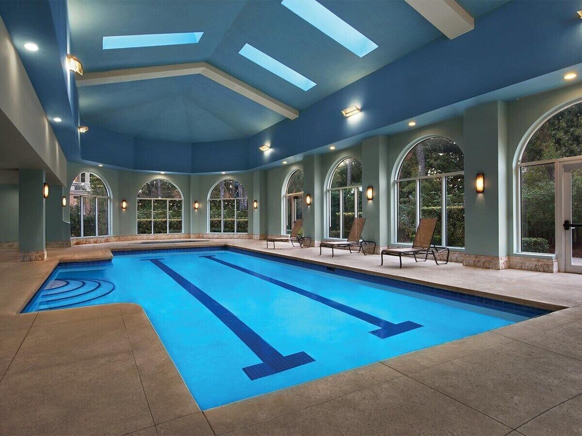 Una piscina interna con acqua cristallina, circondata da poltroncine relax e ampie finestre ad arco.