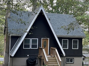 A two-story house with a steeply pitched roof, a front door, and a small porch with steps.